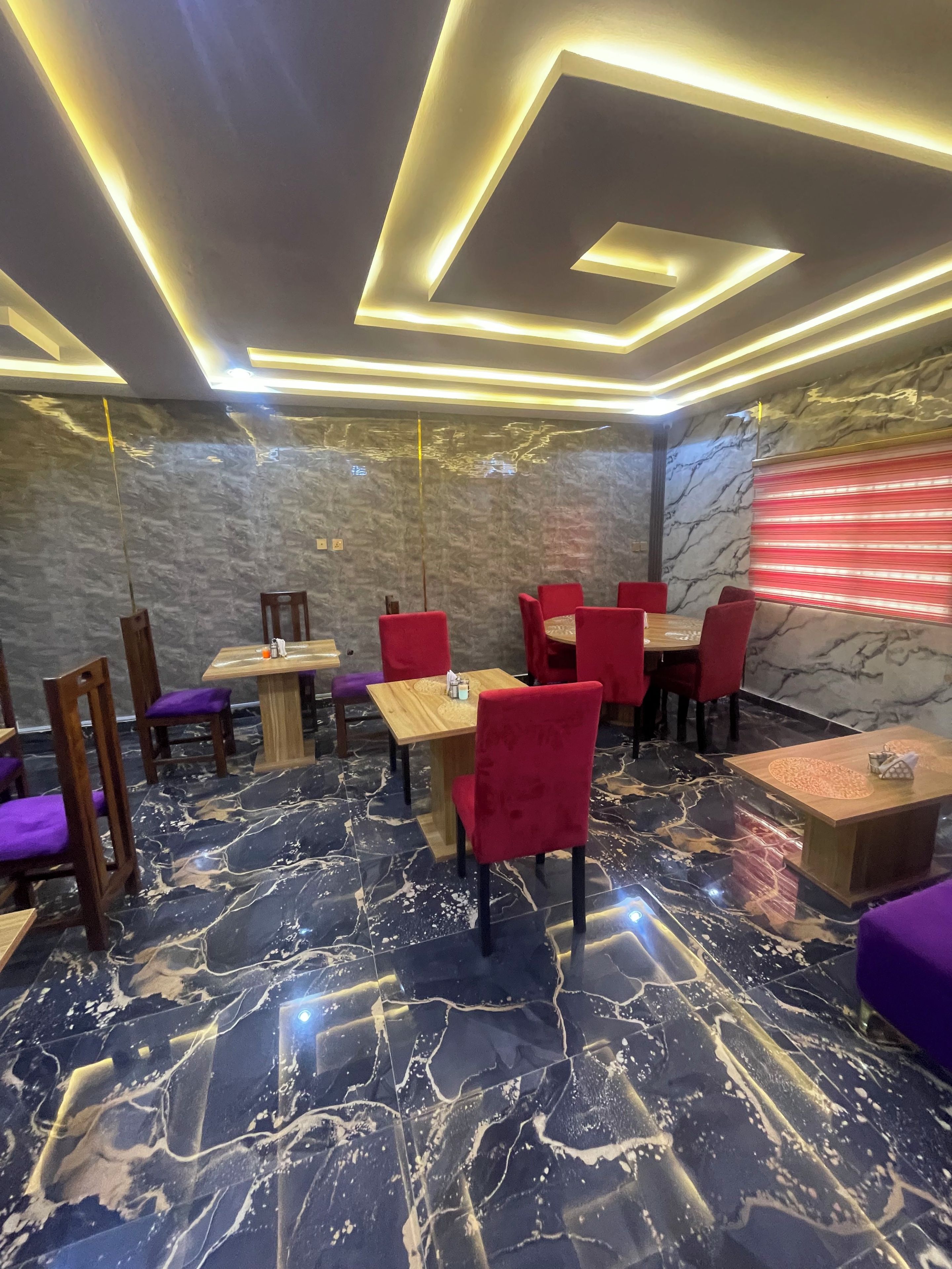 A restaurant interior with marble flooring, red and purple seating, and modern lighting.