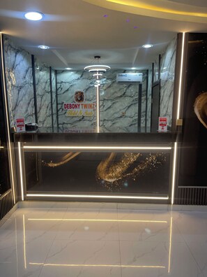 Una recepción con un fondo de pared de mármol, un cartel que dice 'DEBONY TWINZ Hotel & Suite' y una lámpara moderna.