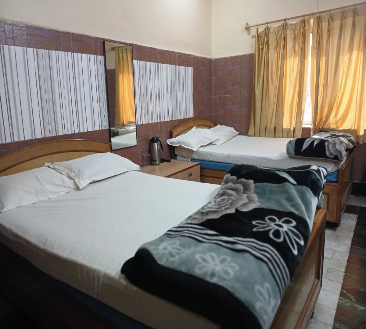 A hotel room with two beds, a nightstand, a mirror, and a window with curtains.