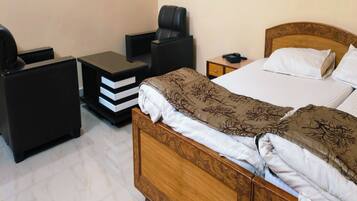 A hotel room with a wooden bed, a bedside table, a chair, and a small desk with drawers.