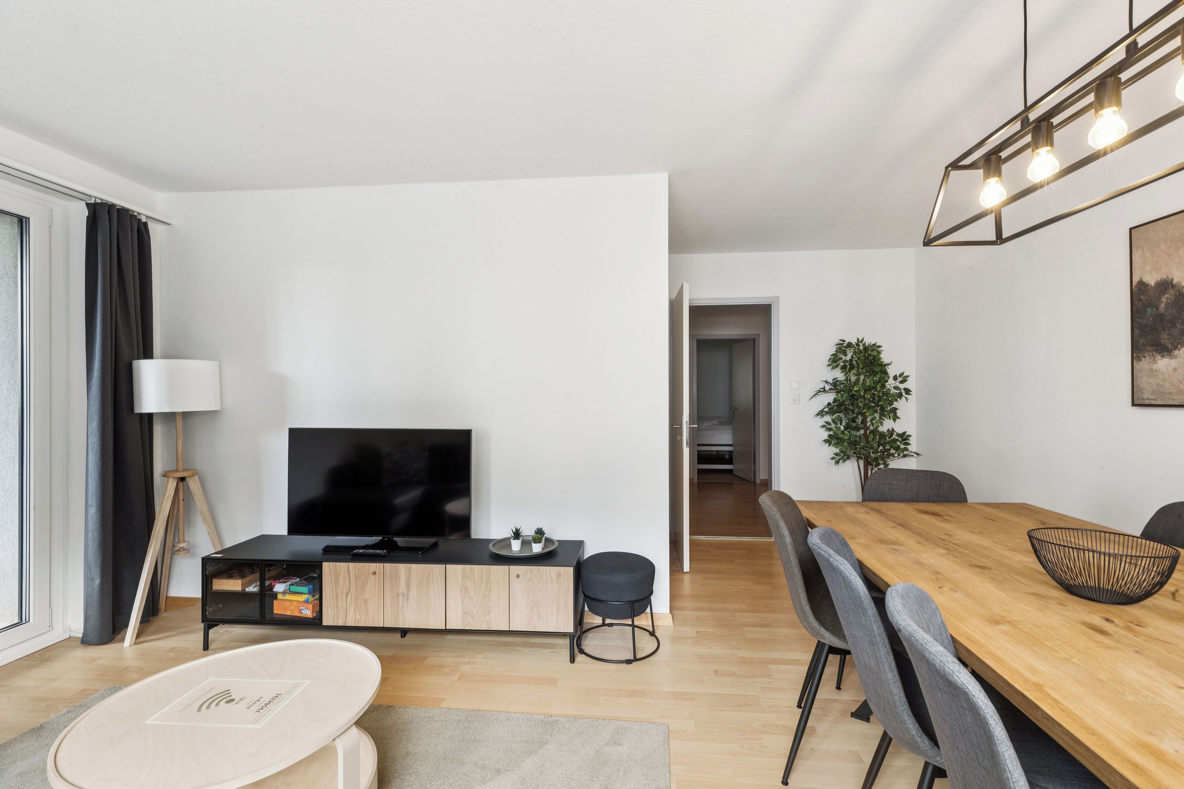 Un salón moderno con televisor de pantalla plana, una mesa de comedor con sillas, una mesa de centro y una planta en maceta.