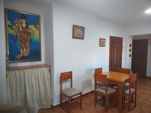 Een eetgedeelte met een houten tafel en stoelen, een schilderij aan de muur en een deur op de achtergrond.