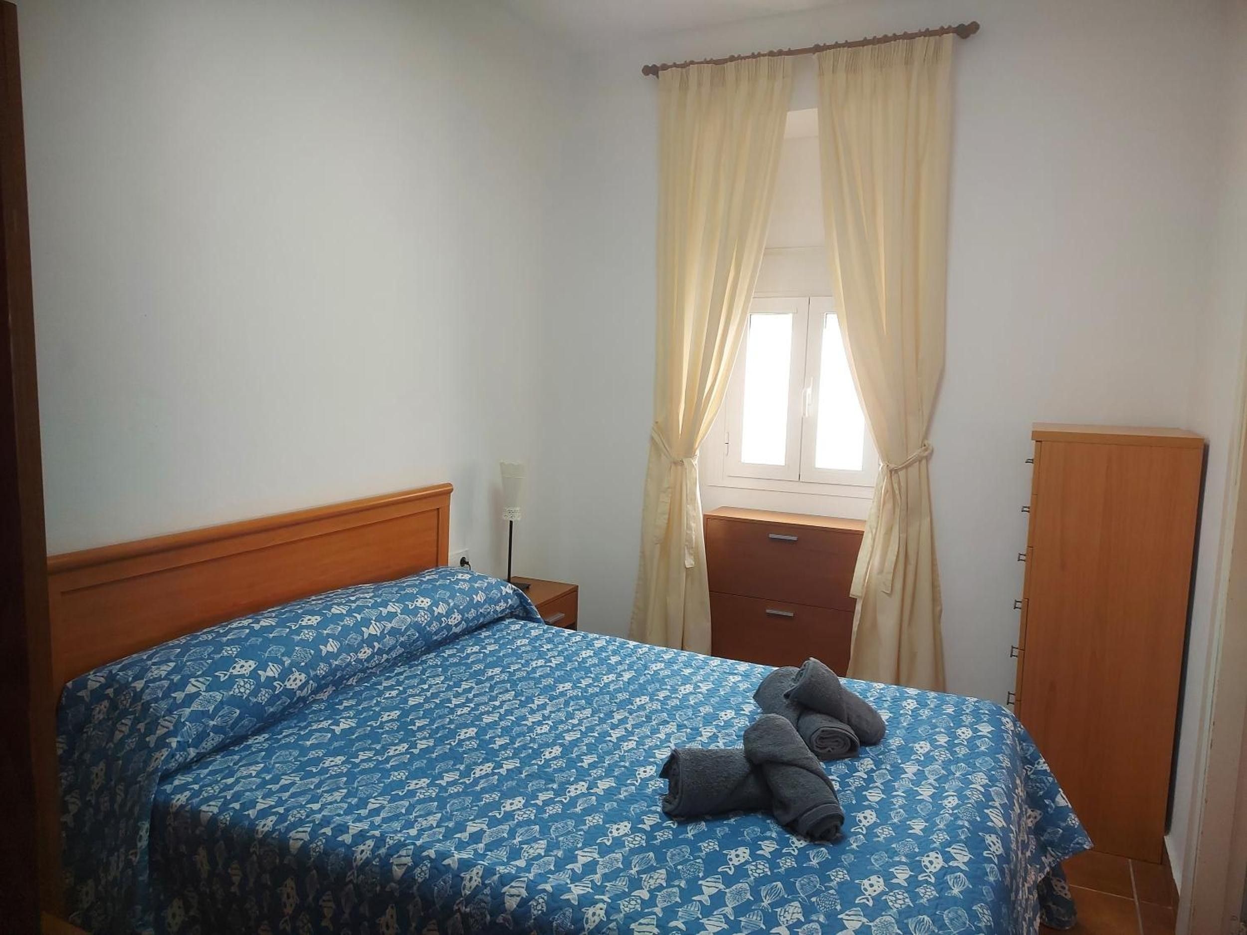 Een slaapkamer met een bed, nachtkastje, kast en een raam met gordijnen.
