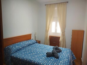 Een slaapkamer met een bed, nachtkastje, kast en een raam met gordijnen.