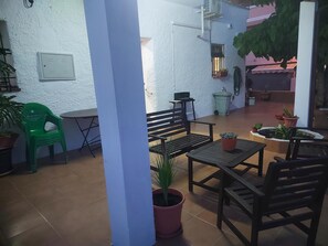 Een terras buiten, met een tafel, stoelen, potplanten en een wandlamp.