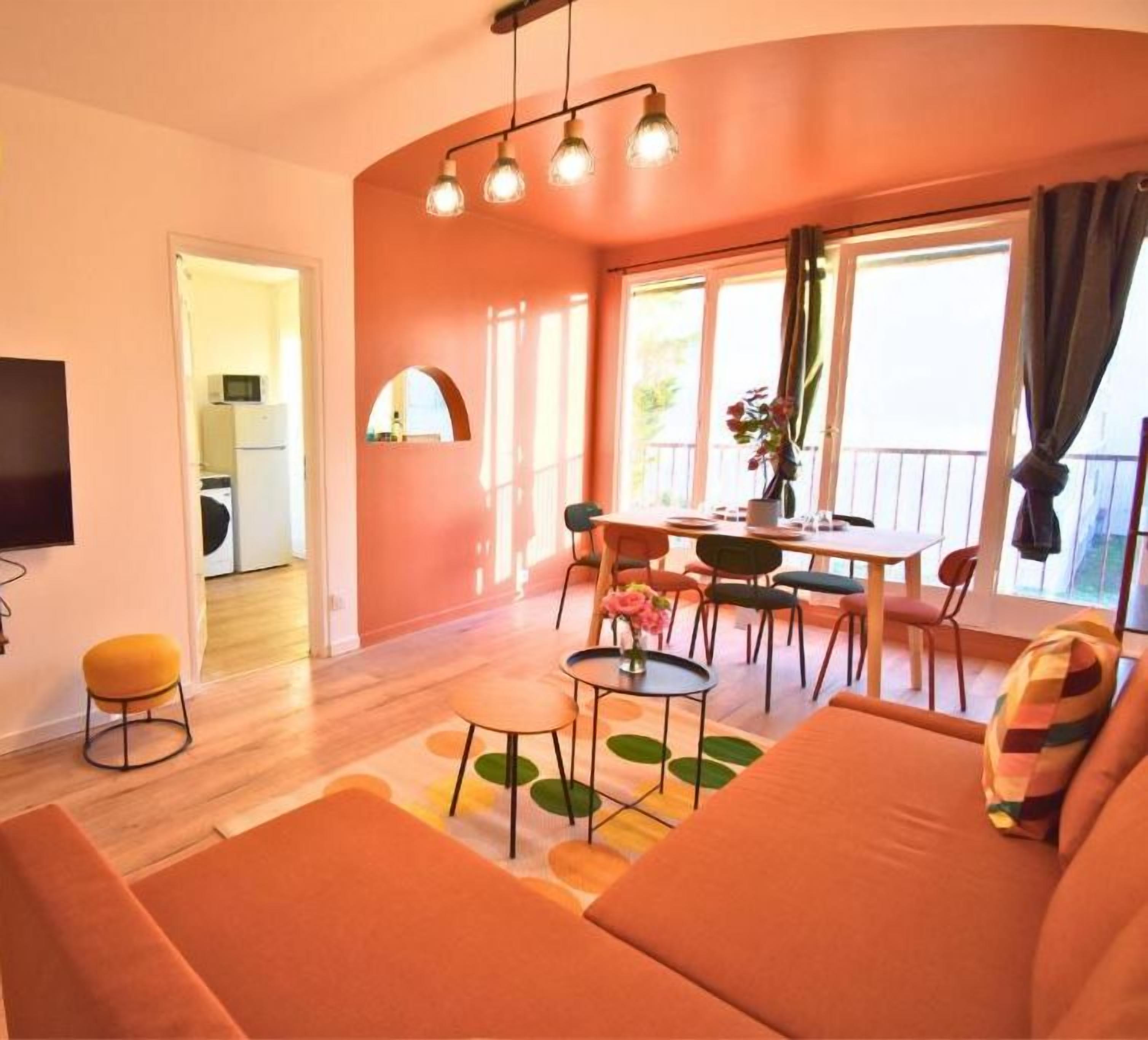 Una sala de estar con sofá, una mesa de comedor y una televisión. Se ve una cocina al fondo.
