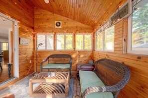 A cabin interior with wooden walls, a dining area, and a seating area with wicker furniture.