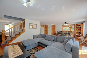 A spacious living area with a large sectional sofa, a wooden staircase, and a dining area with wooden chairs and a table.