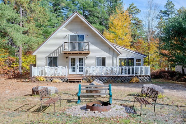 A two-story cabin with a balcony, surrounded by a wooden deck and a fenced yard.
