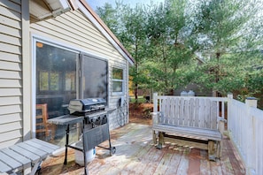 A deck with a grill and outdoor seating, surrounded by trees.