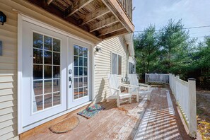 A wooden deck with white chairs and a bench, a front door with glass panels, and a white picket fence.