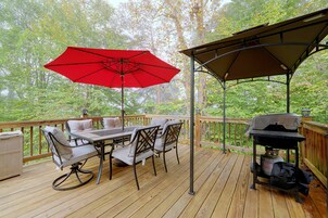 Una terraza de madera con mesa y sillas, un paraguas rojo y una parrilla.