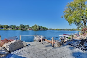 Un muelle frente al lago con barcos, un patio de piedra y vistas a casas al otro lado del agua.