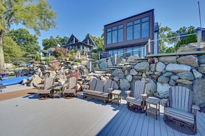 Una terraza de madera con sillas Adirondack, un muro de piedra y un edificio moderno con grandes ventanales.