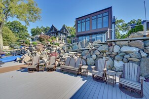 Una terraza de madera con sillas Adirondack, un muro de piedra y un edificio moderno con grandes ventanales.