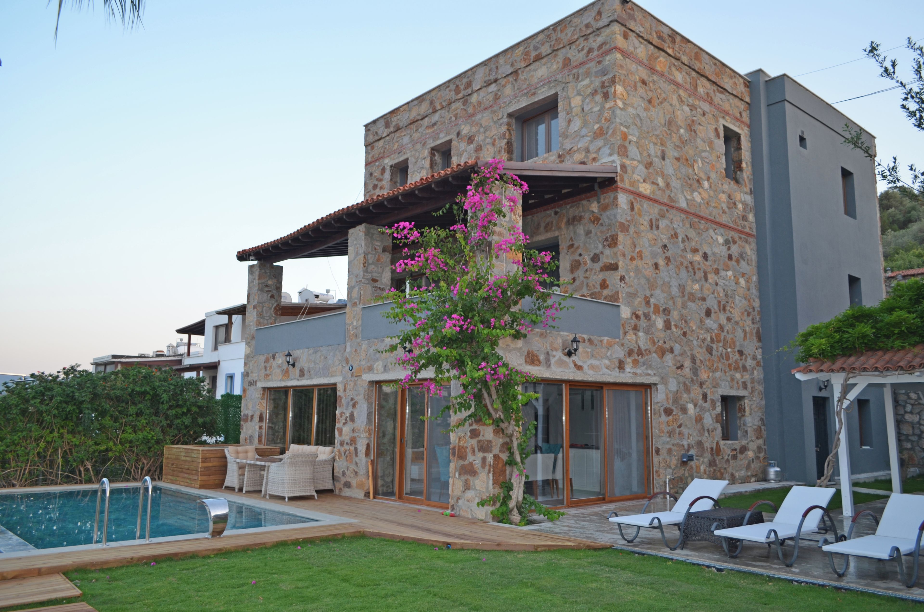 A stone building with a pool, outdoor seating, and a pergola with flowers.