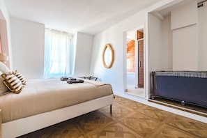 Une chambre à coucher avec un lit, un téléviseur et une vue sur une zone carrelée, visible à travers une porte ouverte.