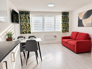 Un salon moderne avec un coin repas, comprenant un canapé rouge, une table à manger avec des chaises et un téléviseur fixé au mur.