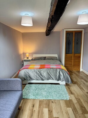 Un dormitorio con cama, mesita de noche, lámpara, armario y un pequeño sofá.