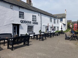 Un edificio blanco con el letrero 'QUEENS ARMS' y terraza al aire libre con bancos.