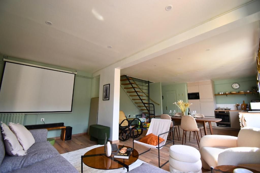Ein stilvolles Wohnzimmer mit einer Couch, Sesseln, einem Couchtisch und einer Projektionsleinwand.