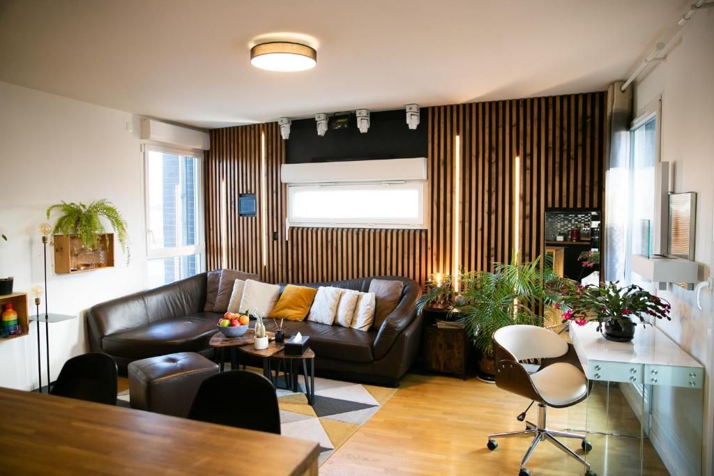A modern living room with a brown leather sofa, a dining table, and a workspace with a desk and chair.