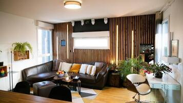 A modern living room with a brown leather sofa, a dining table, and a workspace with a desk and chair.