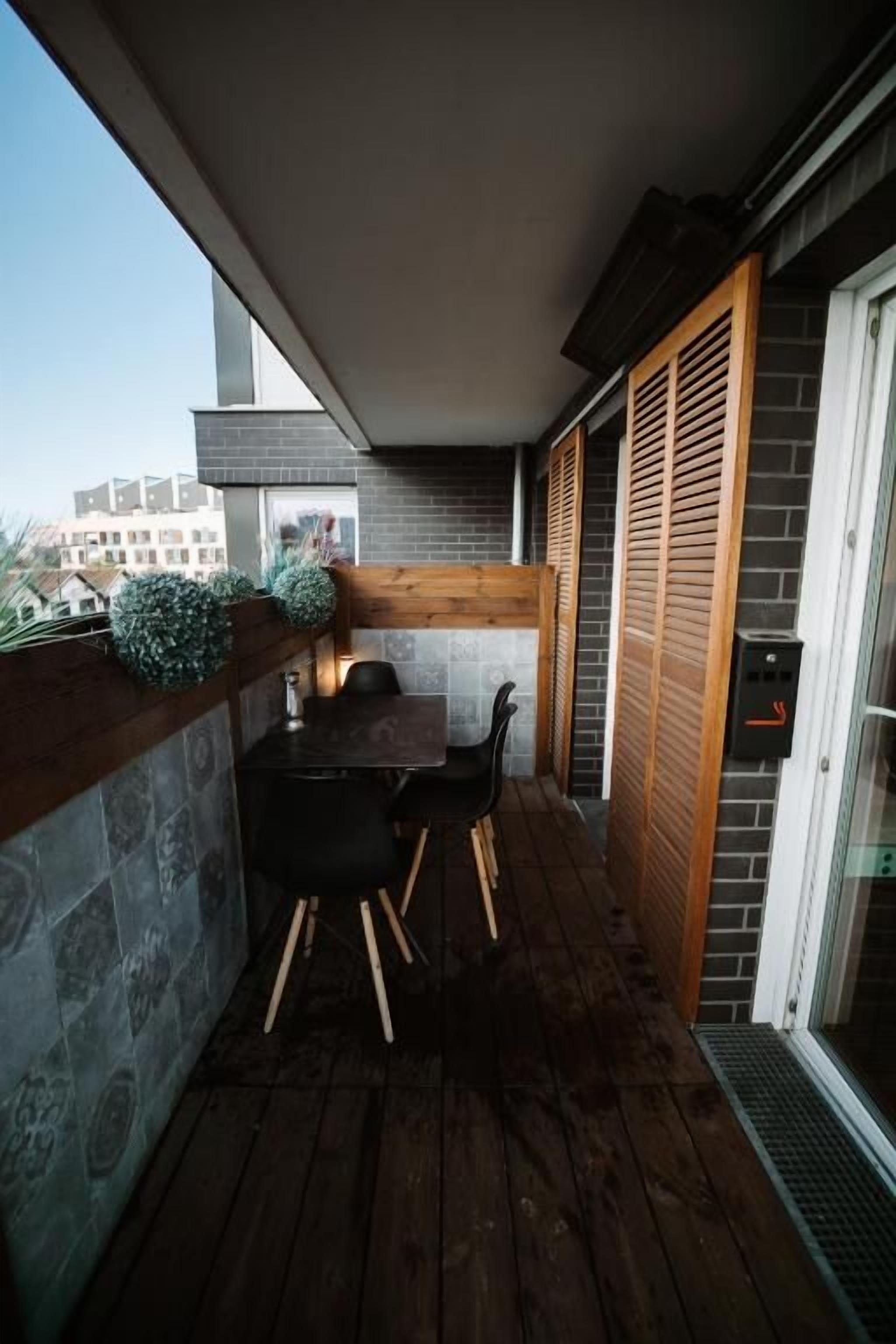 A balcony with a wooden table and chairs, a stone wall, and a sliding glass door.