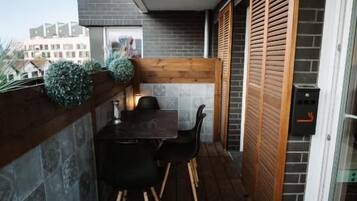 A balcony with a wooden table and chairs, a stone wall, and a sliding glass door.
