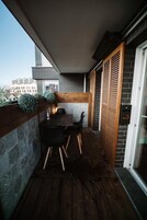 Un balcón con una mesa y sillas de madera, un muro de piedra y un ventanal corredero.