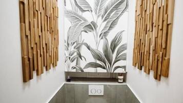 A narrow bathroom with a toilet, a trash bin, and a toilet paper holder. The walls have a vertical wooden panel design.