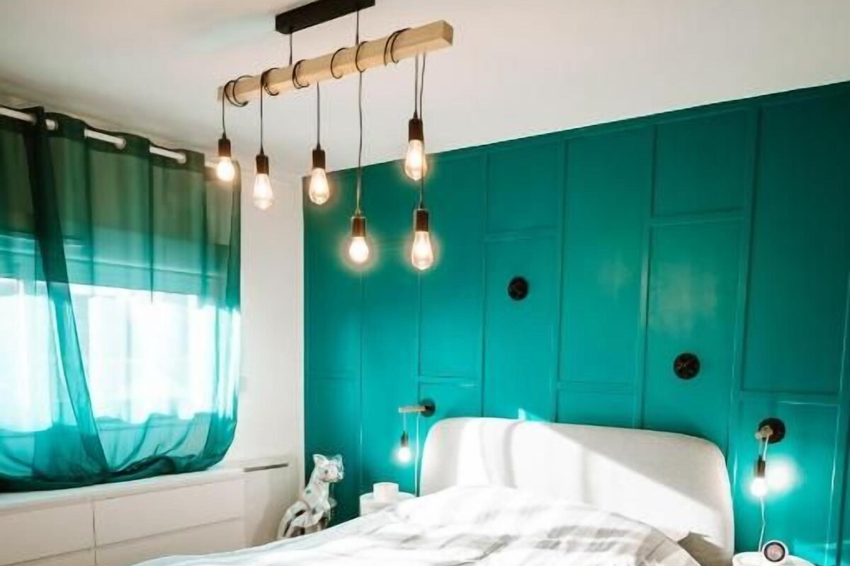 A bedroom with a bed, bedside lamps, and a teal accent wall.