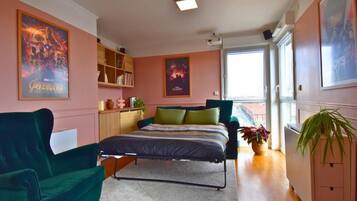 Ein Schlafzimmer mit einem Bett, einem grünen Sessel, einem Bücherregal und einem Fenster.