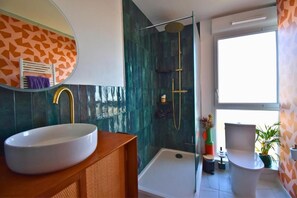 Un baño moderno con un lavabo ovalado grande, una ducha a pie y un inodoro.