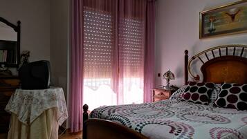 Un dormitorio con una cama de madera, una mesita de noche con una lámpara, una silla y una ventana con cortinas.