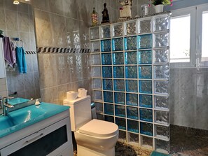 Een badkamer met een marmeren wand, een douchecabine van glas, een wit toilet en een blauwe wastafel.