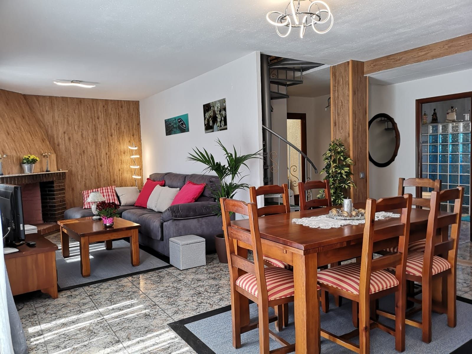 Una sala de estar moderna con chimenea, una zona de comedor con sillas de madera y una escalera que sube a un piso superior.