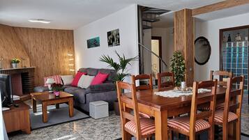 Una sala de estar moderna con chimenea, una zona de comedor con sillas de madera y una escalera que sube a un piso superior.