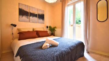 Ein Schlafzimmer mit einem Bett, einem großen Fenster, einer Topfpflanze und einem Wandspiegel.