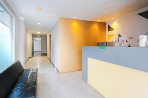 Et hotellets receptionsområde med en bænk, en disk og en væg med lodrette skodder.