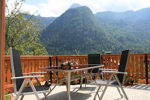 En udendørs terrasse med et bord og stole, et træhegn og et bjergrigt baggrund.