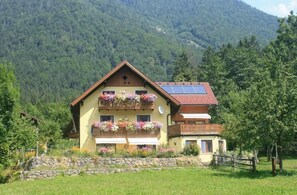 En toetages chalet med skråtag, balkoner med blomsterkasser og en stenvæg foran.