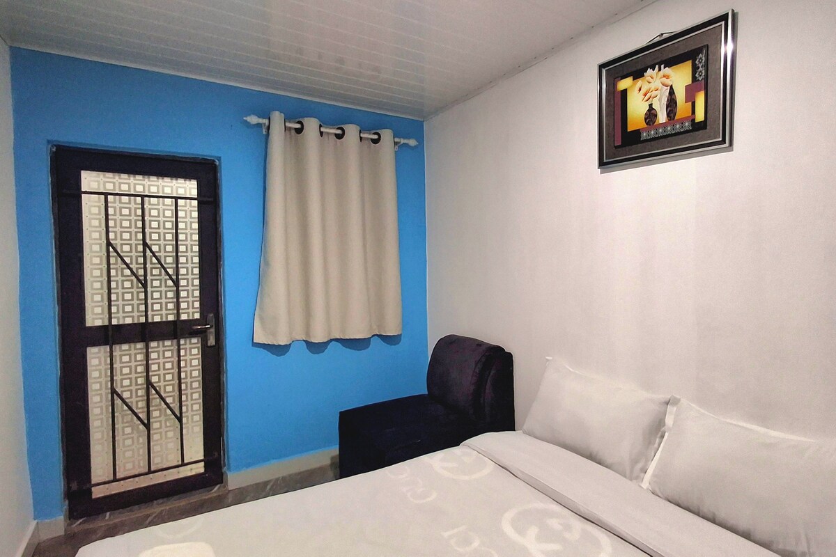 A bedroom with a bed, a window with curtains, a wall-mounted picture, and a door with a metal grid.