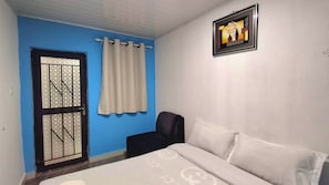 A bedroom with a bed, a window with curtains, a wall-mounted picture, and a door with a metal grid. - Kalebalika Cottages  (Kasama)