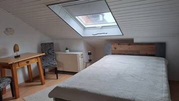 Ein Schlafzimmer mit Dachfenster, einem Bett, einem Schreibtisch, einem Sessel und einem kleinen Tisch mit Lampe.