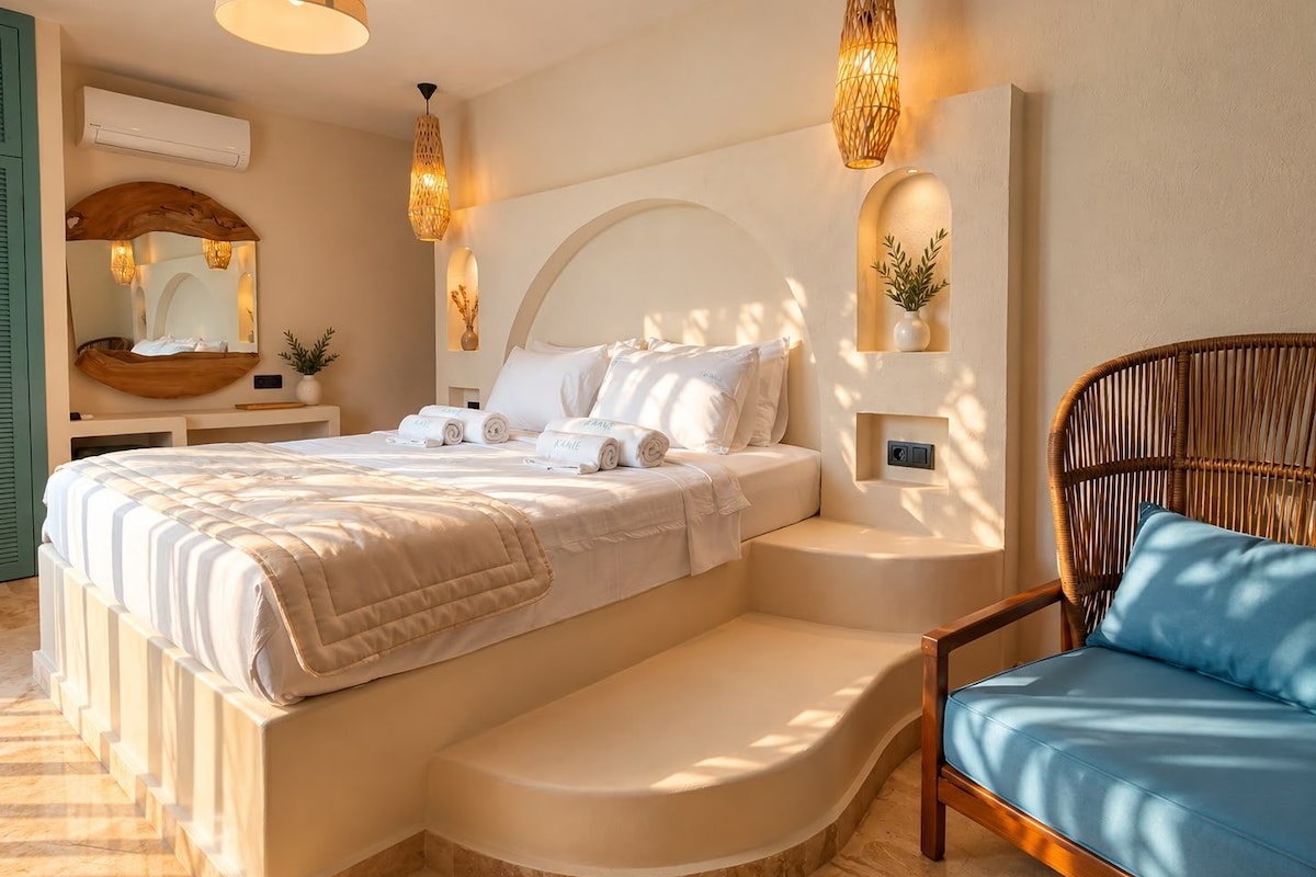 Une chambre à coucher moderne avec un grand lit, une banquette intégrée, un fauteuil en osier et des luminaires fixés au mur.