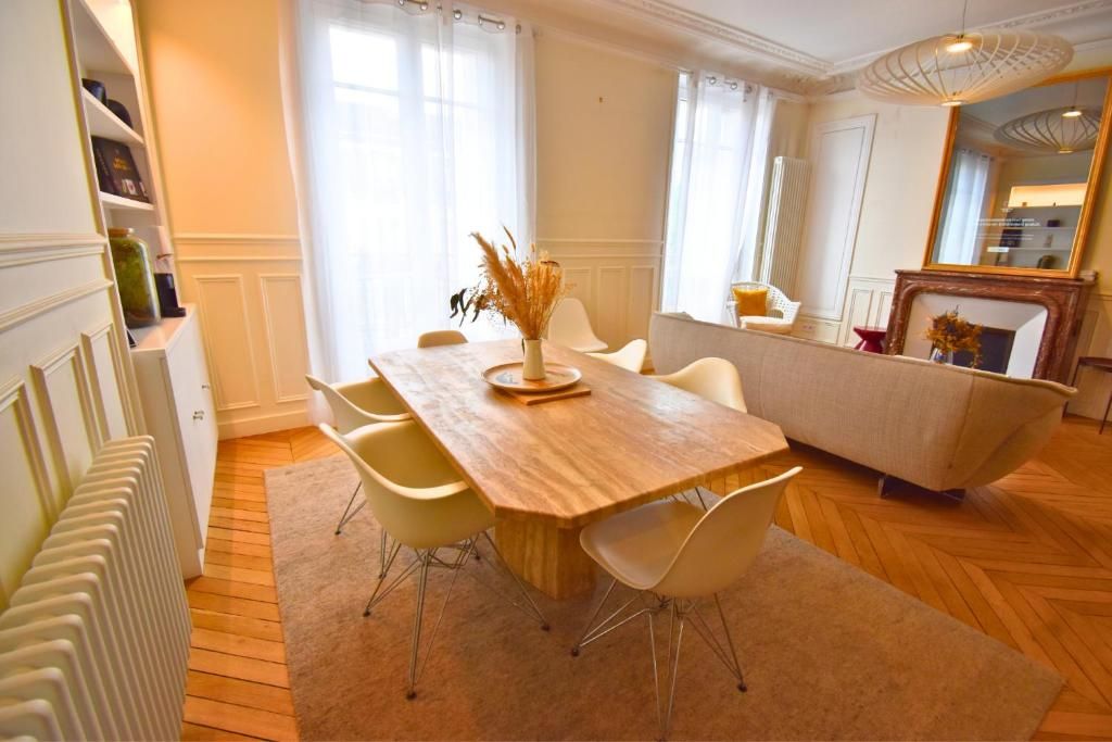 Un coin repas avec une table en bois, des chaises blanches et un vase contenant des plantes séchées.