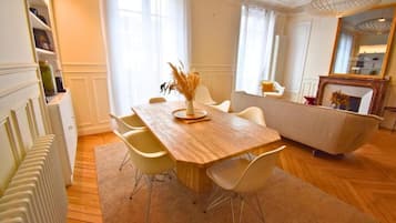 Un coin repas avec une table en bois, des chaises blanches et un vase contenant des plantes séchées.