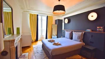 Une chambre d’hôtel comprenant un lit, une table de chevet, un miroir et une étagère murale avec des livres.