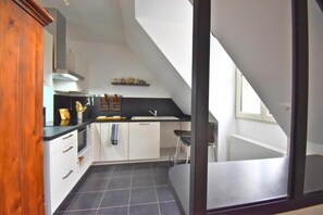 A kitchen with a black countertop, white cabinets, a black tiled floor, and a window with a view. - Senlis - Éclat d'Époque (Senlis)
